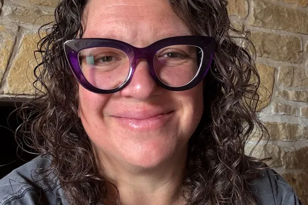 person with brown curly hair and black glasses smiling