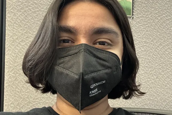 person with black hair wearing a black mask with posters behind them