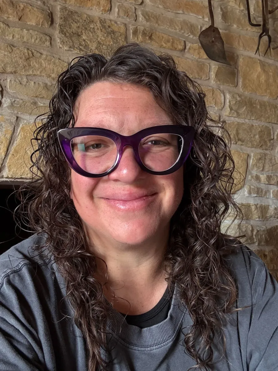 person with brown curly hair and black glasses smiling